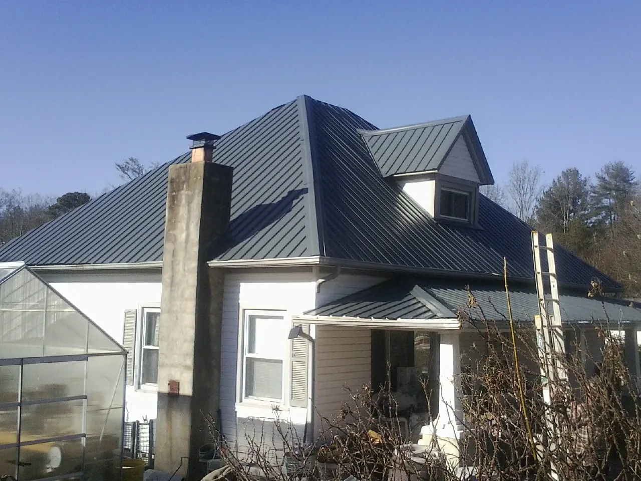 Dark blue standing seam metal roof on a white farmhouse with dormer — Slate & Tile Roof Repair by Roofing Brothers in Rich Square