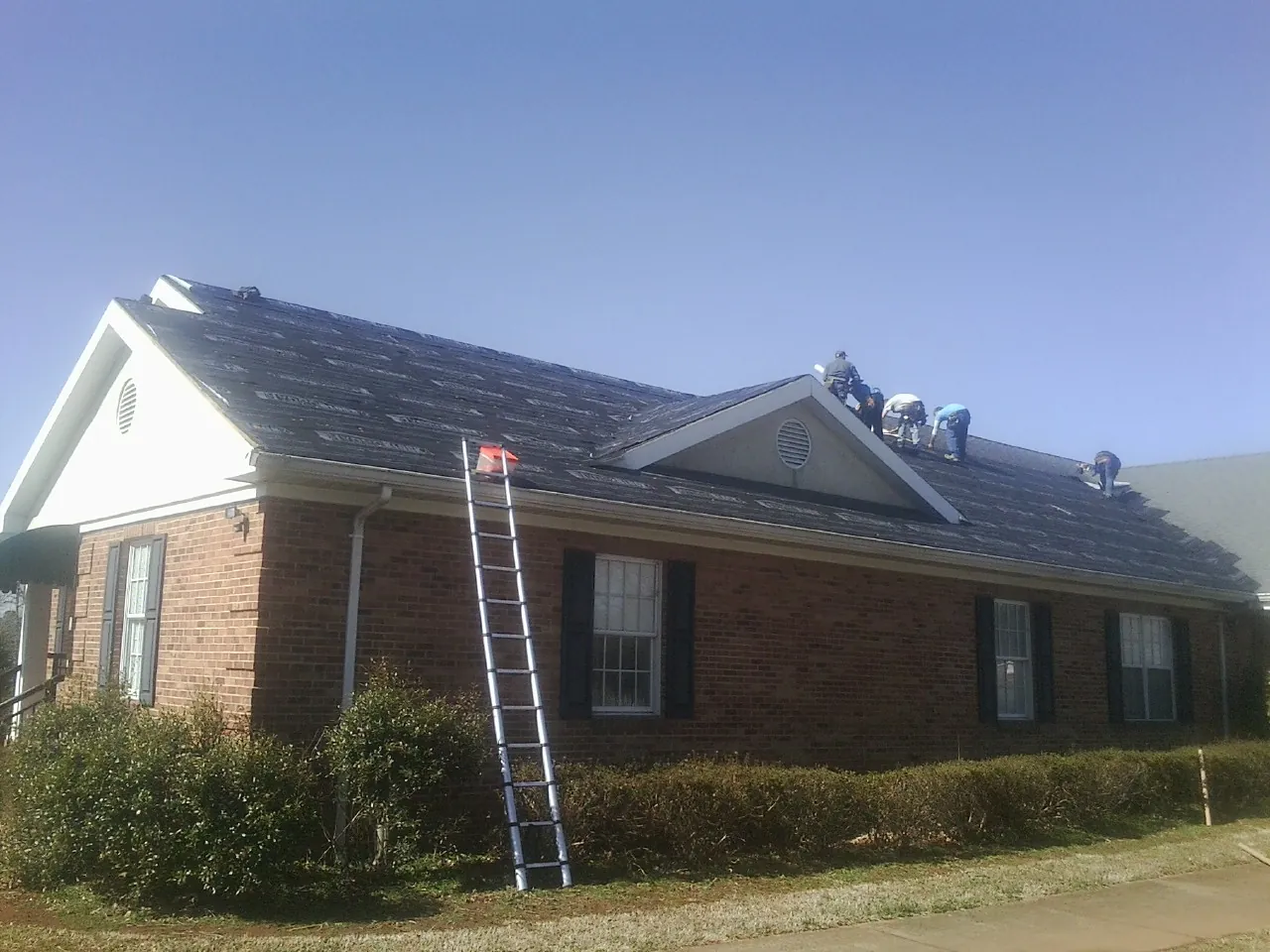Crew tearing shingles off a brick ranch roof with a ladder set — Metal Roof Repair work by our crew in Rich Square