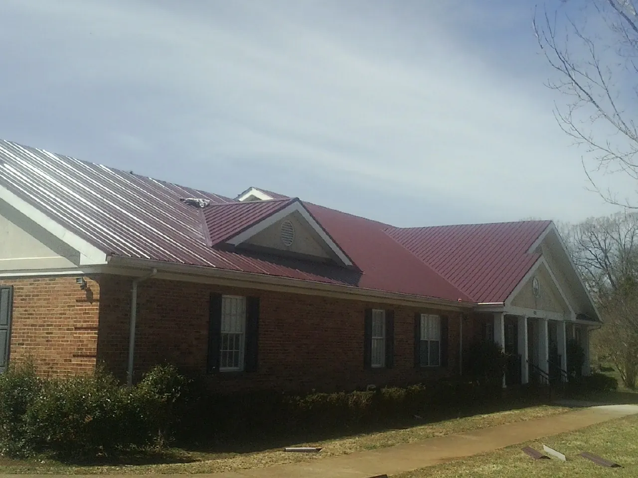 Red metal roof with gabled entries on a long brick building, from a Hail Damage Roof Repair job in Rich Square