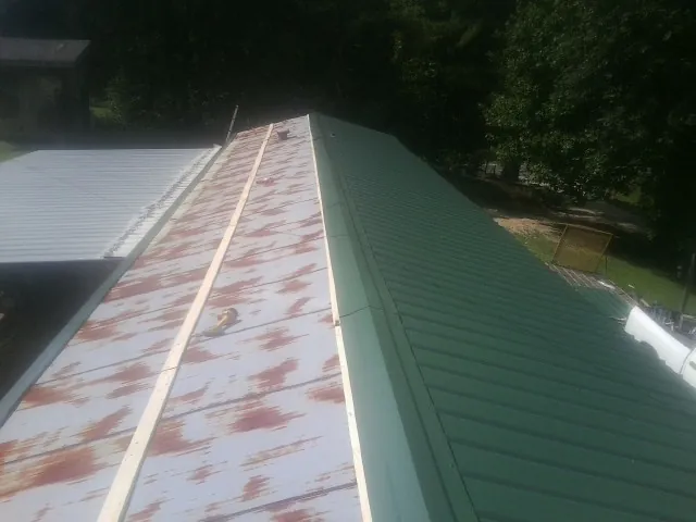 Old rusted panels beside newly installed green metal roofing — Wind Damage Roof Repair by Roofing Brothers in Rich Square