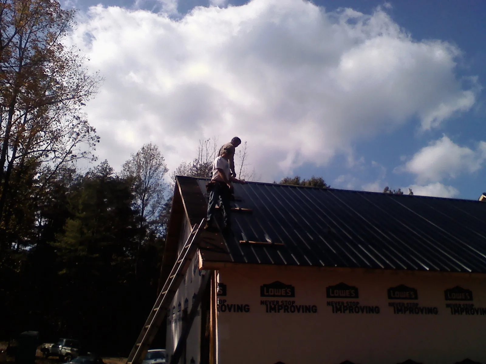 Roofer fastening dark metal panels high against a cloudy sky, from a Roof Inspection job in Rich Square