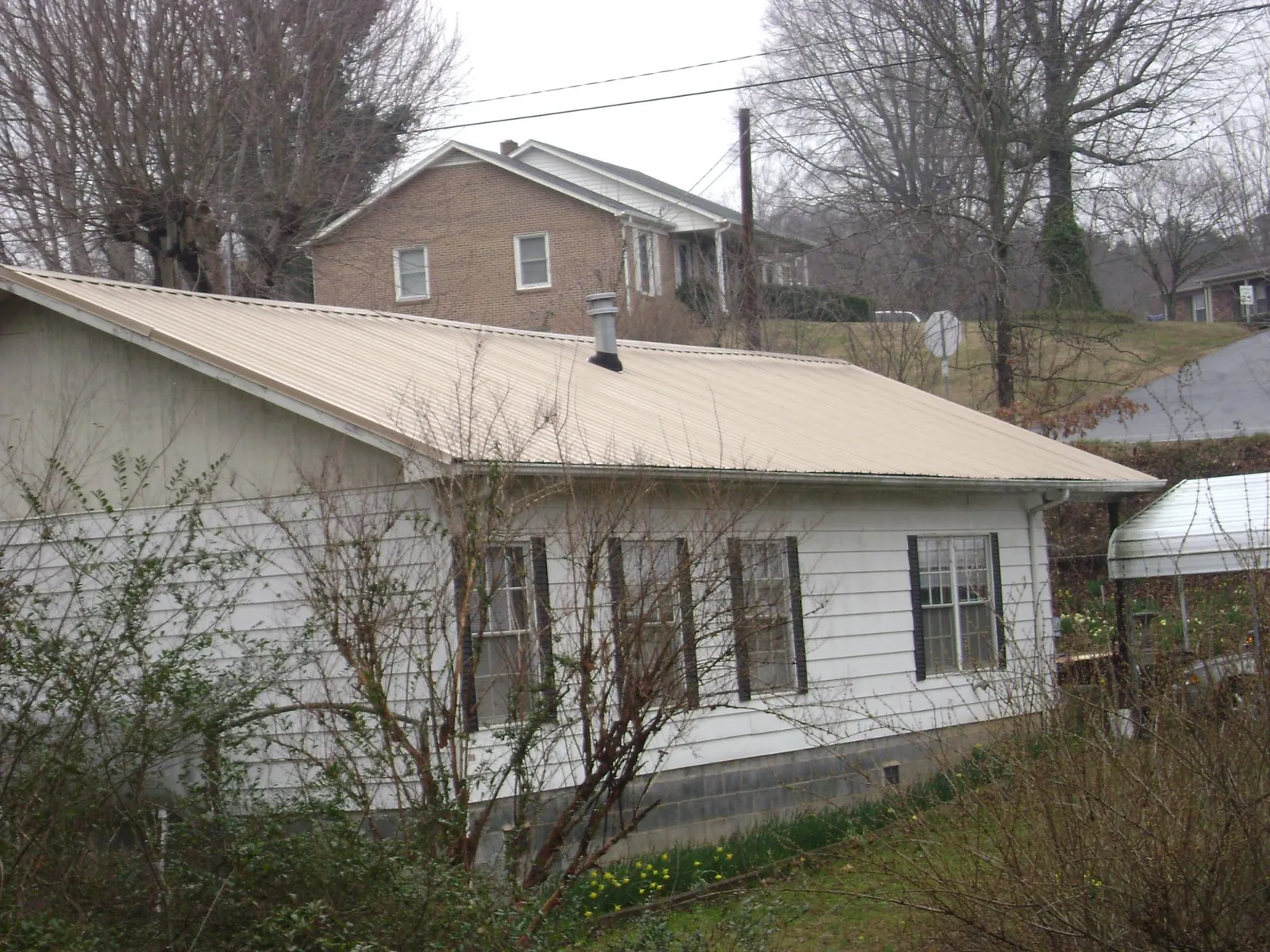 Tan metal roof on a white sided house set into a hillside — Commercial Roofing by Roofing Brothers in Rich Square